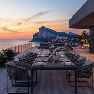 Ein schön gedeckter Tisch steht auf einer Terrasse firekt am Meer. Im Hintergrund sind ein paar Felsen und der Sonnenuntergang zu sehen