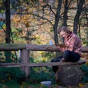 Innehalten & Reflektieren – Resilienz beginnt im Miteinander Person sitzt in herbstlicher Natur mit Notizblock und Tasse – Symbol für Reflexion, Ruhe und Selbstführung im Teamkontext.