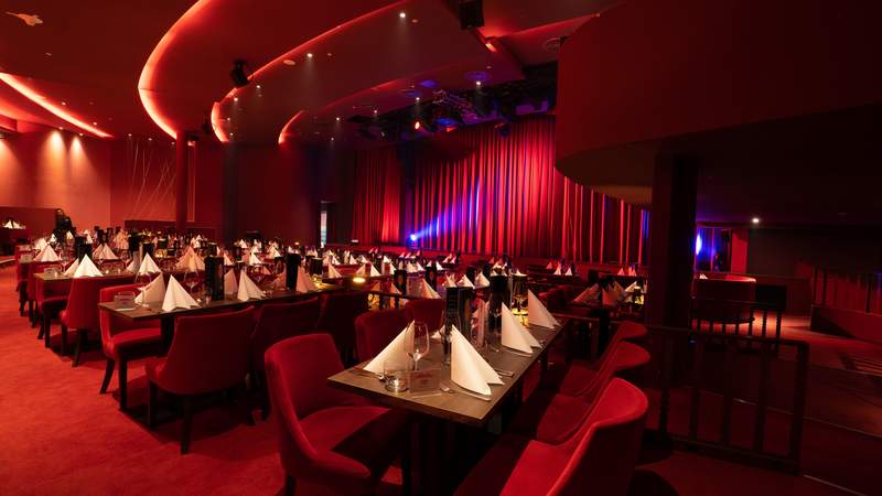 Sicht von hinten auf den roten Theatersaal mit Blick auf die Bühne und die eingedeckten Tische.