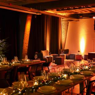 Weihnachtsfeier "Weihnachtlicher Orient" Festlich gedeckte Tafel für eine Weihnachtsfeier mit elegant arrangierten Gläsern und Tellern, umgeben von warmem Kerzenschein und verschwommenen, leuchtenden Weihnachtslichtern im Hintergrund in Form von Sternen und Bäumen.