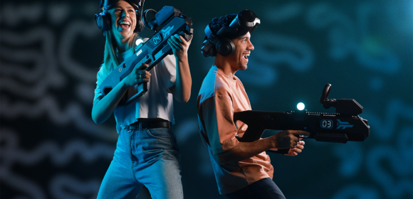 Eine Frau und ein Mann tragen Virtual Reality Brillen und Gewehrcontroller und lachen.