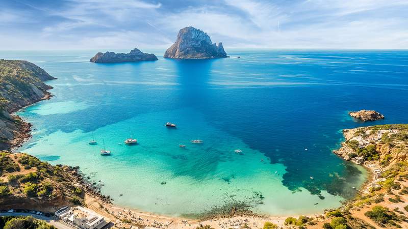 Man sieht eine blaue Bucht mit Felsen und Strand