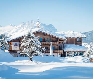 Verschneites Hotel im Bauernhaus Stil in Fieberbrunn mit Bergkulisse im Hinergrund