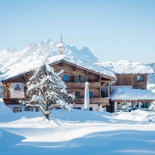 Verschneites Hotel im Bauernhaus Stil in Fieberbrunn mit Bergkulisse im Hinergrund