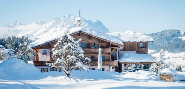 Hotel & Chalets Großlehen Verschneites Hotel im Bauernhaus Stil in Fieberbrunn mit Bergkulisse im Hinergrund