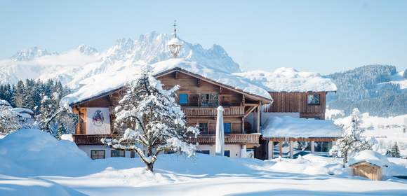 Verschneites Hotel im Bauernhaus Stil in Fieberbrunn mit Bergkulisse im Hinergrund