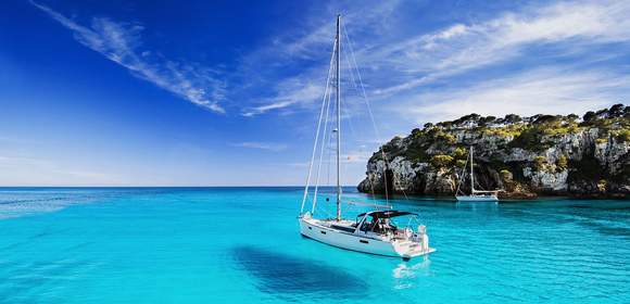 ein Segelboot schwimmt auf hellblauem Wasser vor einer Felsenküsten