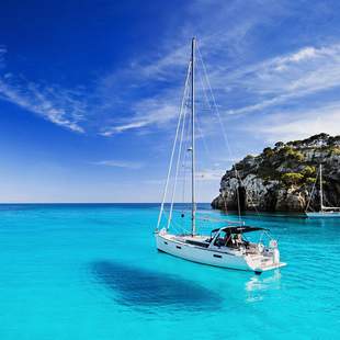 ein Segelboot schwimmt auf hellblauem Wasser vor einer Felsenküsten