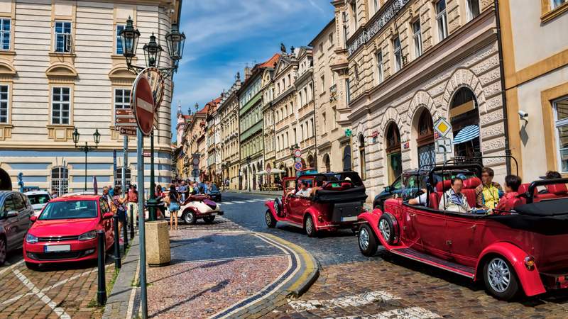 Gäste fahren mit roten Cabrio Oldtimern durch ein altes Stadtviertel.