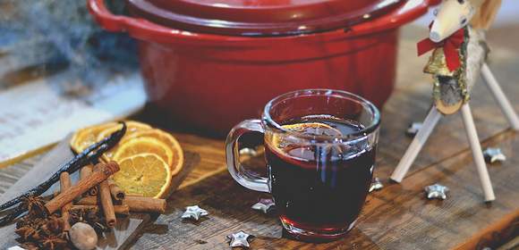 Ein roter Topf mit einem Glas Glühwein und Zimtstangen sowie Orangenscheiben